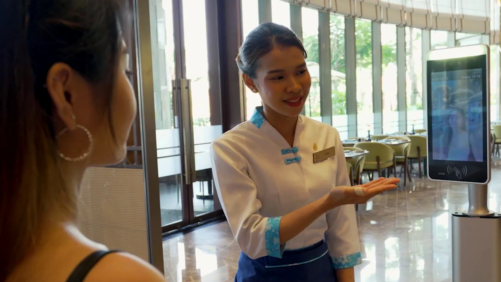 Hotel guest facing a real face-verification terminal while a hotel team member assists